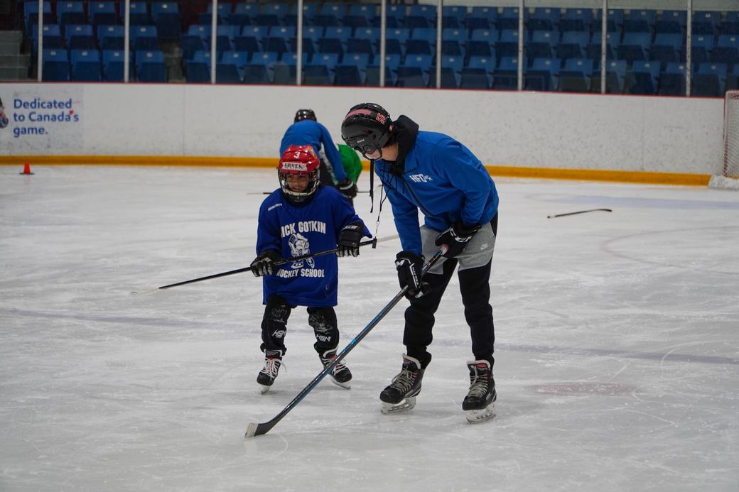 A coach working one to one with a camper in the corner of the rink