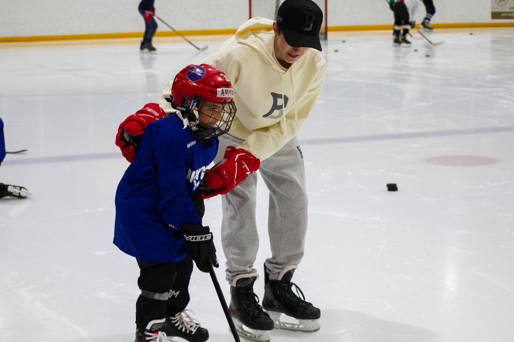 A coach in a cream hoodie working with a camper in a red helmet