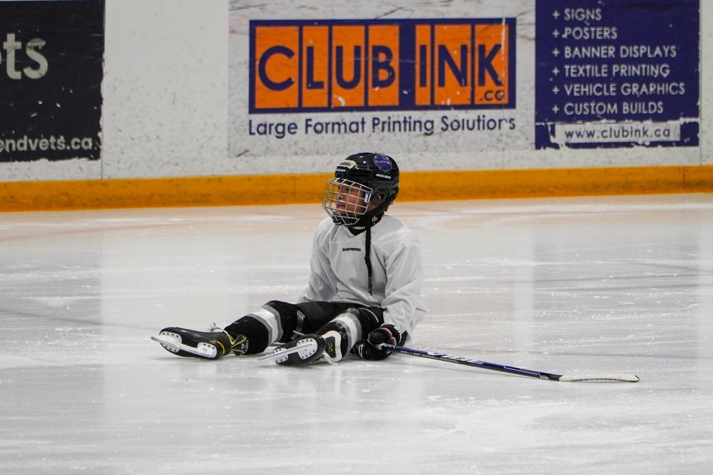 A first-time skater sitting on the ice while a volunteer talks them through standing up