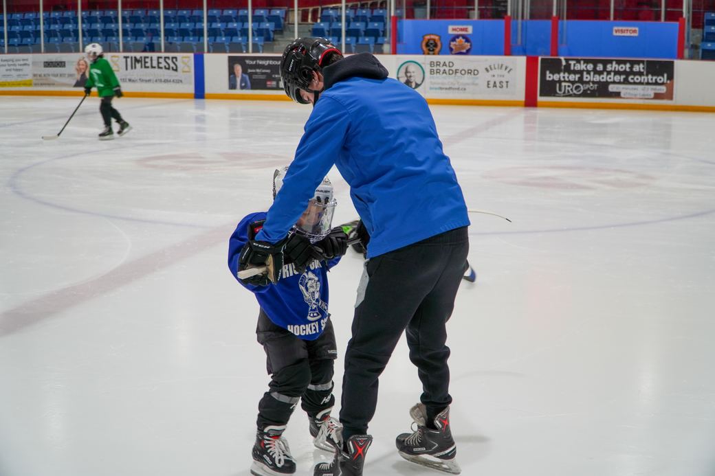 A coach holding both hands of a small camper taking their first strides