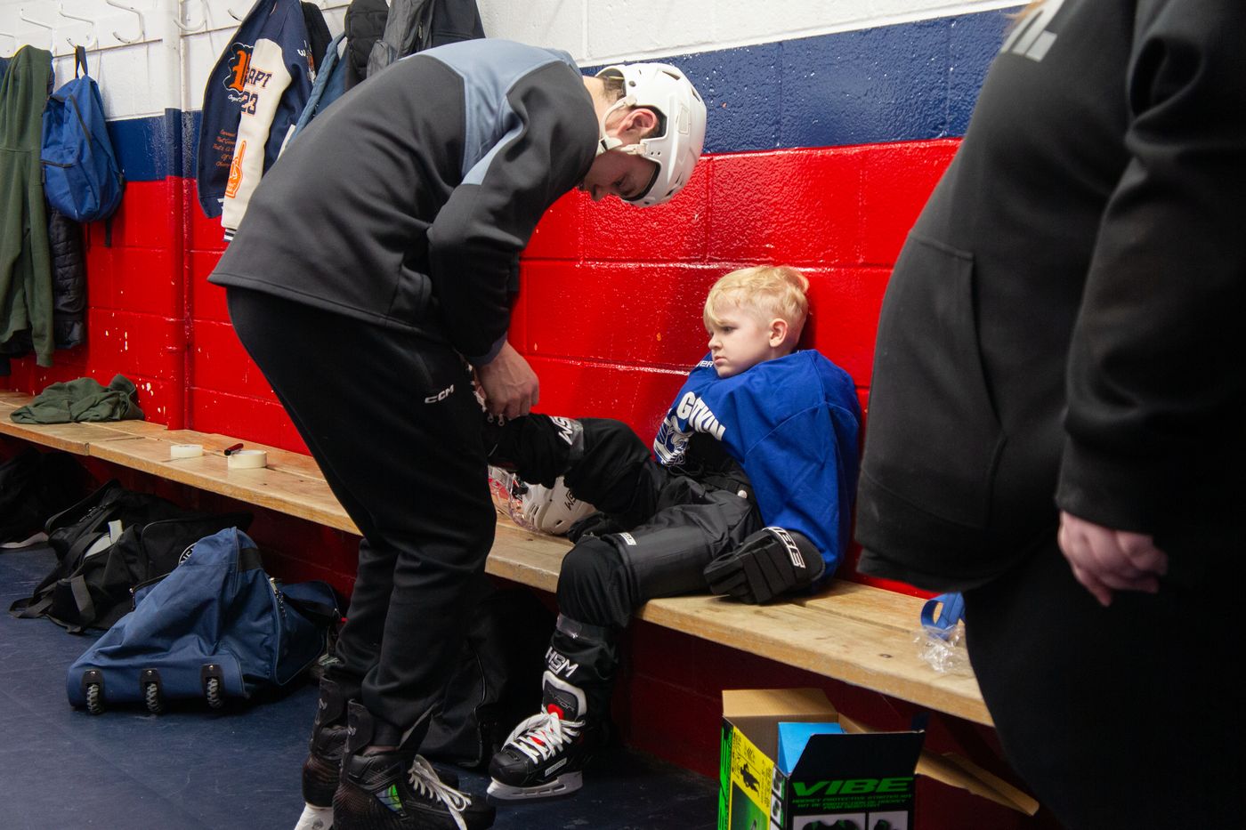 Campers sitting along the bench pulling on skates and shin pads before a session