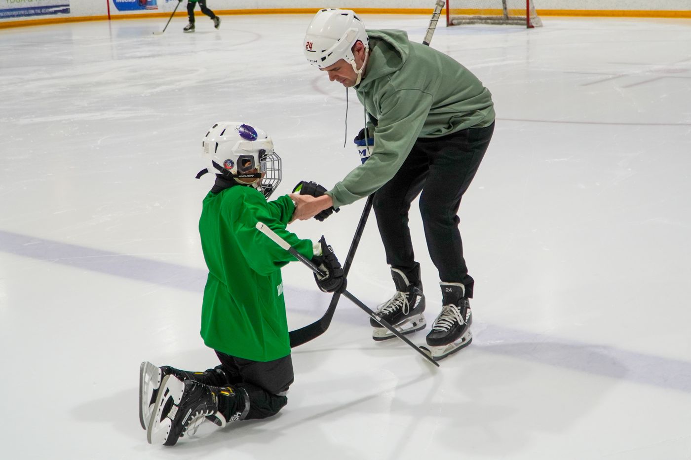 A volunteer steadying a first-time skater who is kneeling on the ice learning to stand up