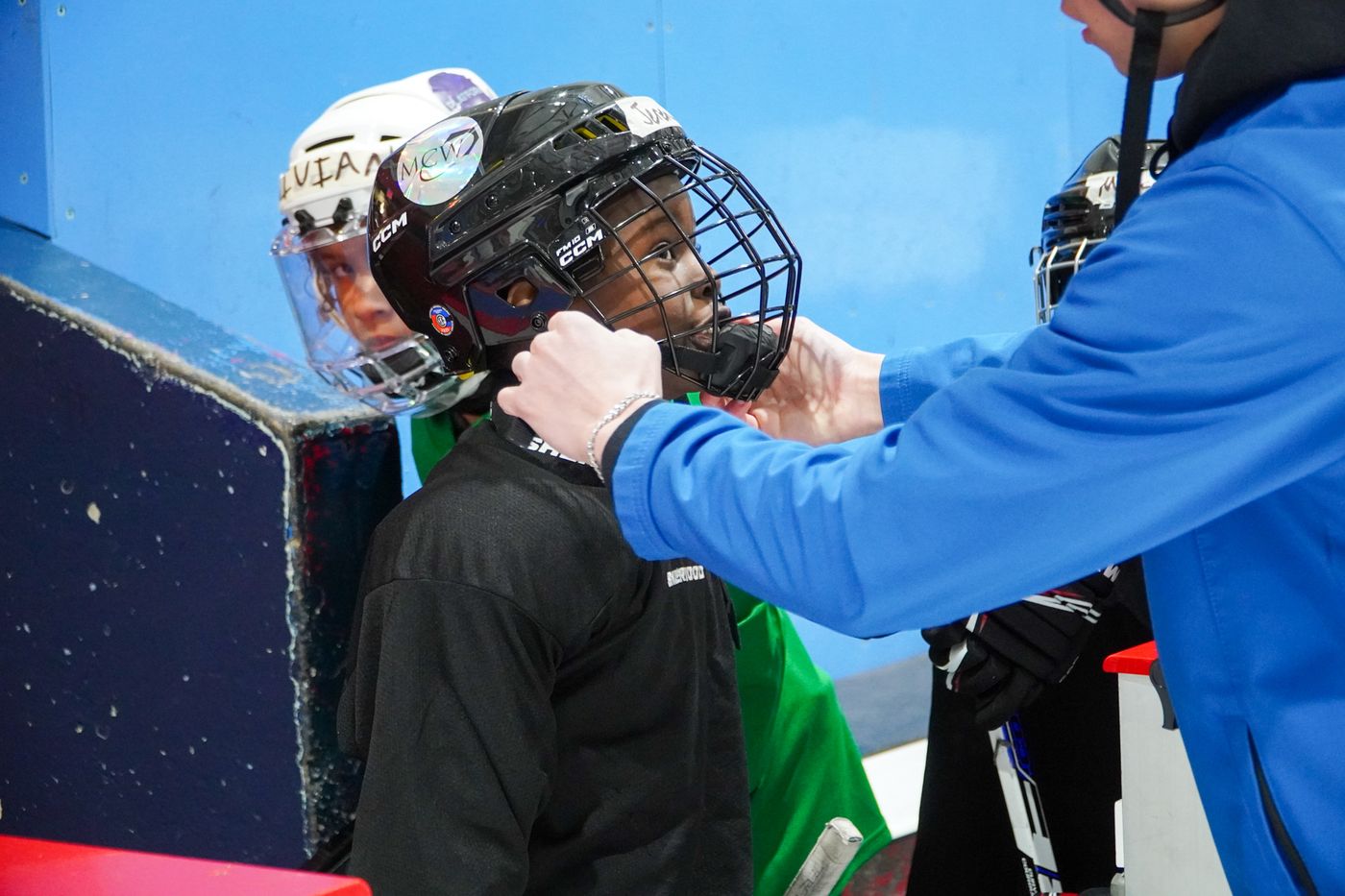 A volunteer fitting a helmet onto a camper at the boards before the camper steps onto the ice