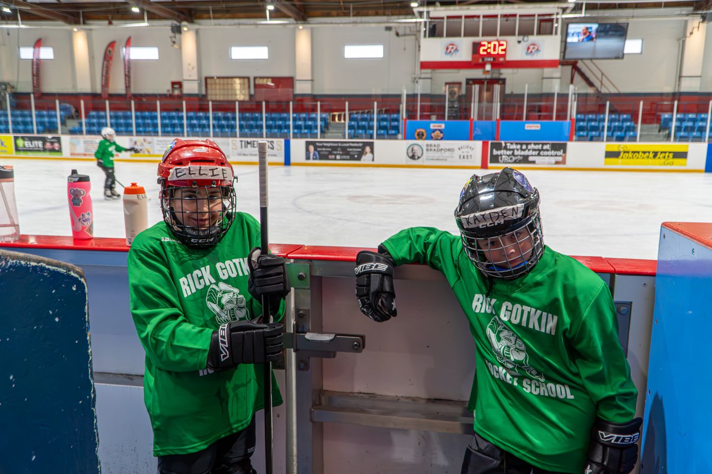 Two campers in green jerseys waiting at the gate to step onto the ice
