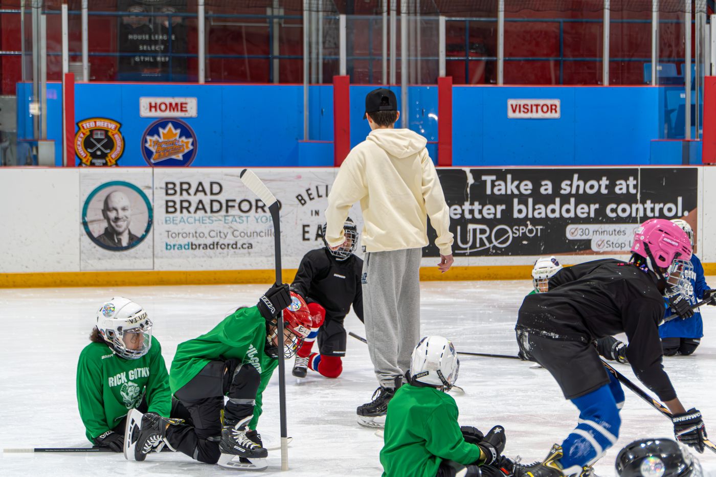 A large group of campers in green and blue jerseys crowded together on the ice with their coaches and volunteers