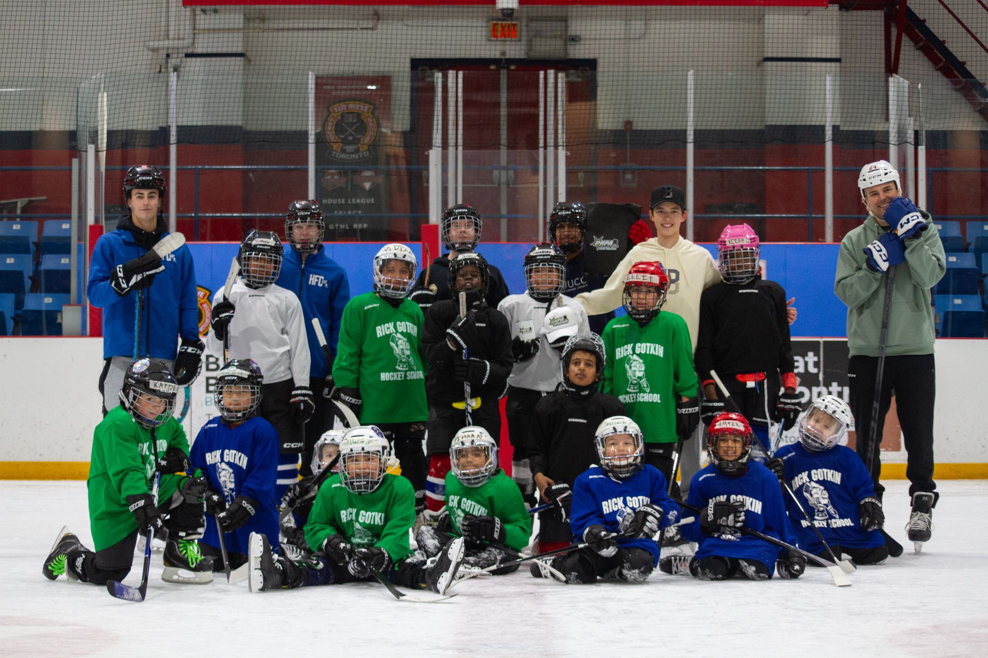Campers and volunteers gathered together on the ice at the end of a March break camp session, arena seating rising behind them