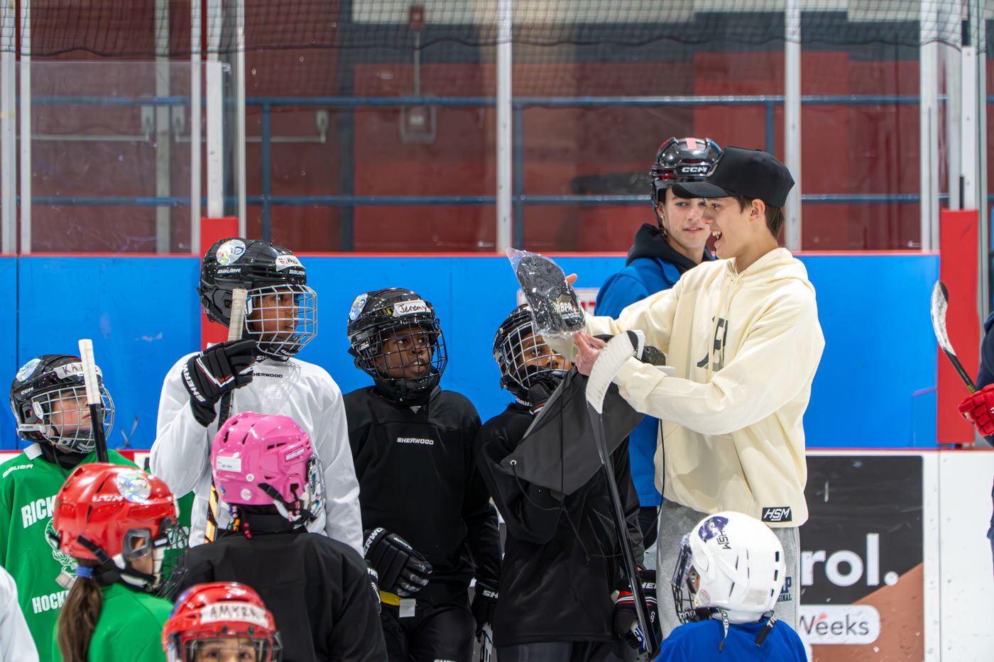 Student volunteers in cream hoodies helping a group of helmeted campers along the boards