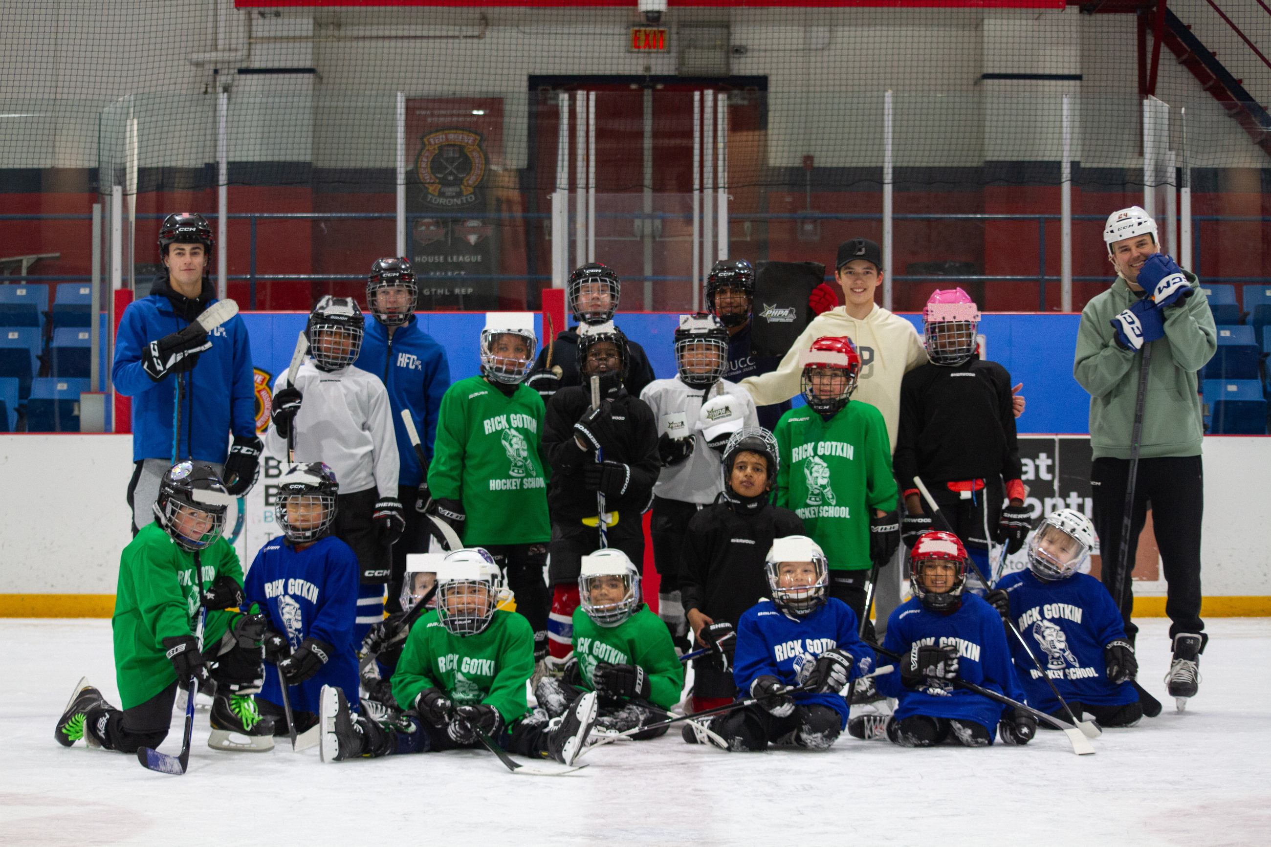 The whole March break camp posed together on the ice at Ted Reeve Community Arena, the youngest campers kneeling at the front in green and blue jerseys and the coaches and student volunteers standing behind