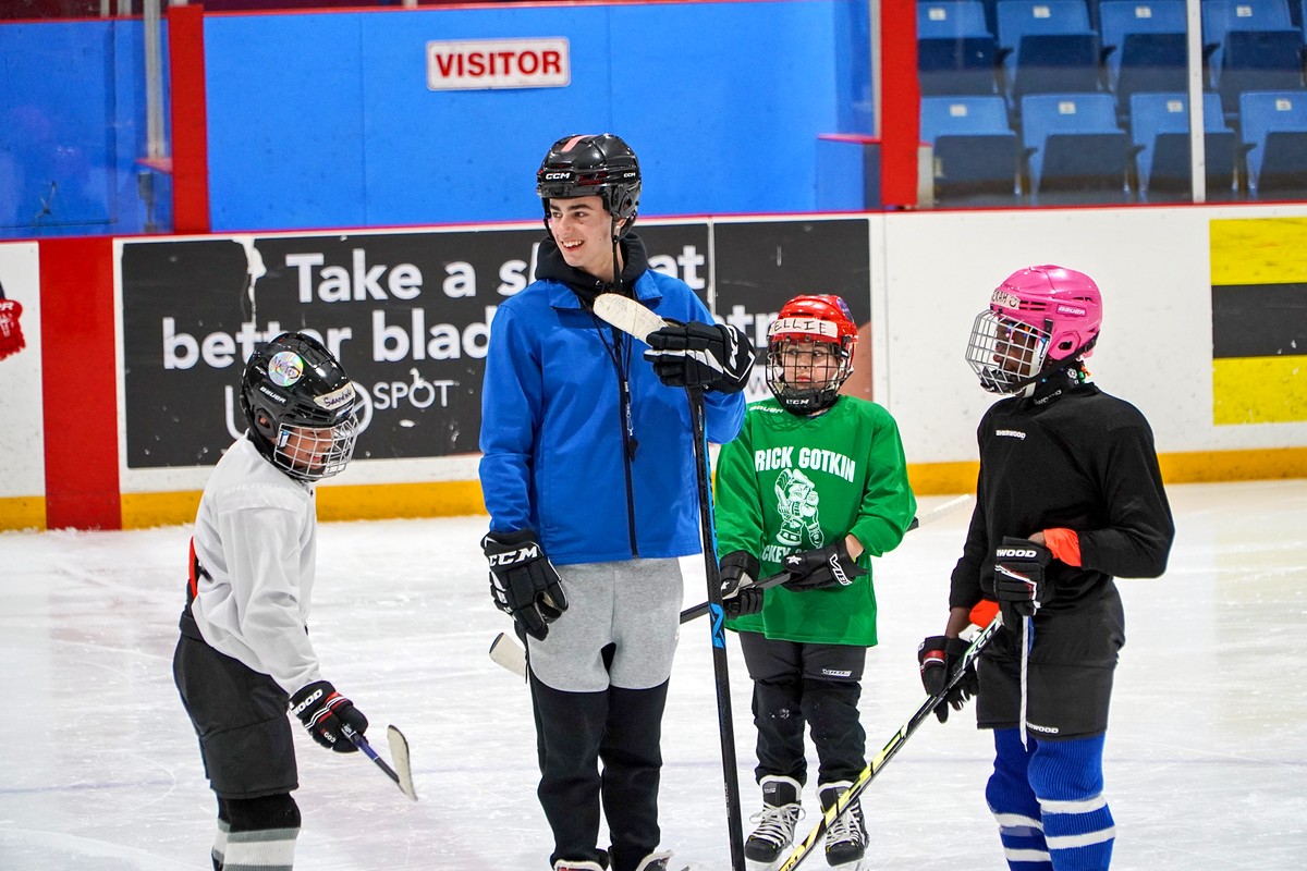 A student volunteer in a blue jacket smiling with campers at the boards