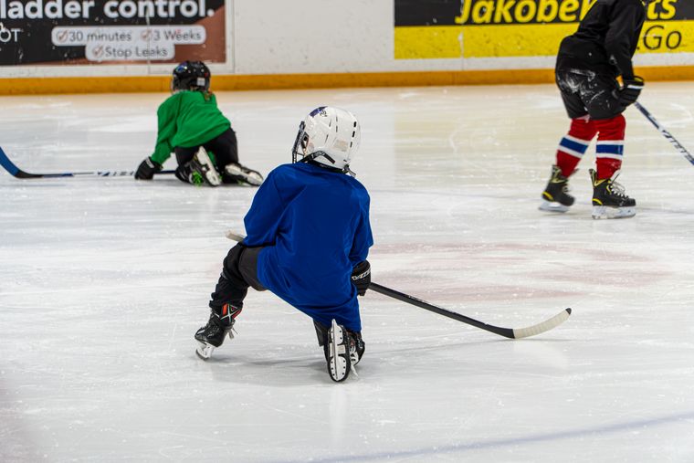 A young camper in a green jersey learning to skate with a volunteer alongside